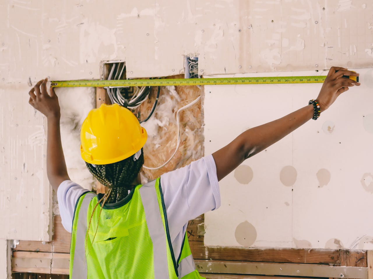 Female construction worker with hardhat and vest measuring an interior wall.